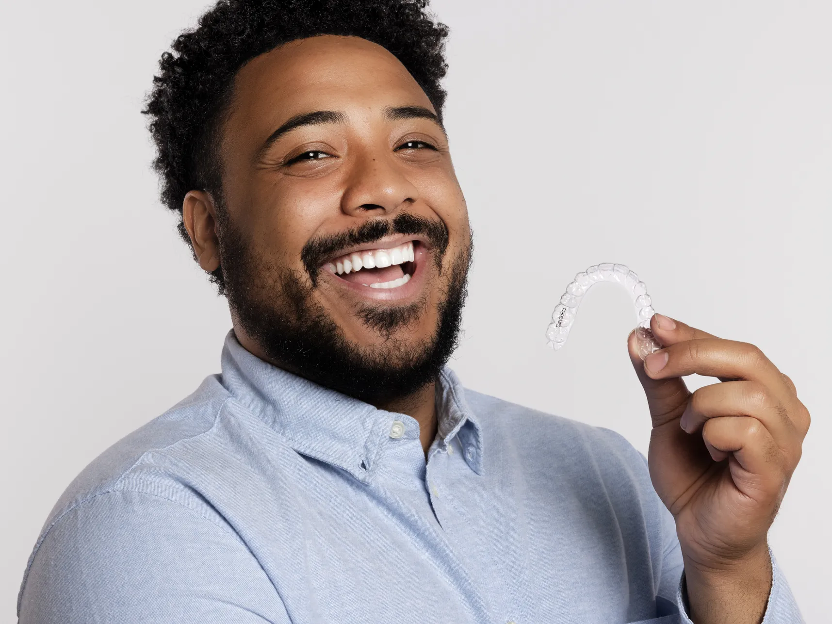 A smiling patient holding a Candid Pro clear aligner