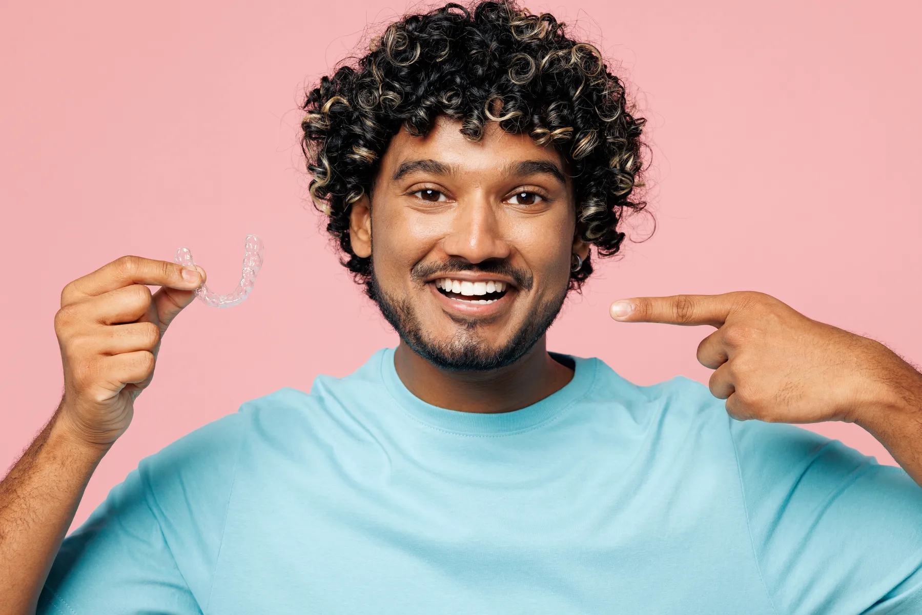 A smiling patient holding an Invisalign clear aligner